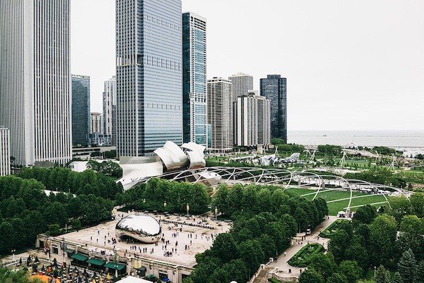 Aerial view of a city skyline with skyscrapers, a large park with green trees, and a body of water in the background