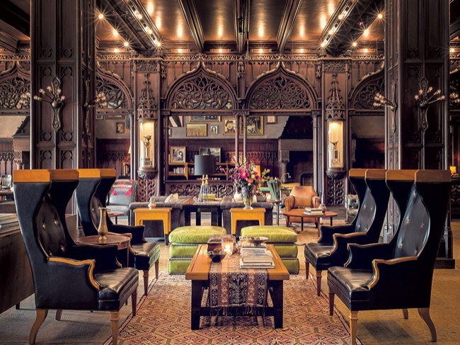 Ornate lounge interior with dark carved wood arches, leather wingback chairs, patterned rug, and warm ambient lighting